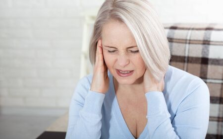 Woman suffering from stress or a headache grimacing in pain as she holds the back of her neck with her other hand to her temple, with copyspace. Concept photo with indicating location of pain.の写真素材