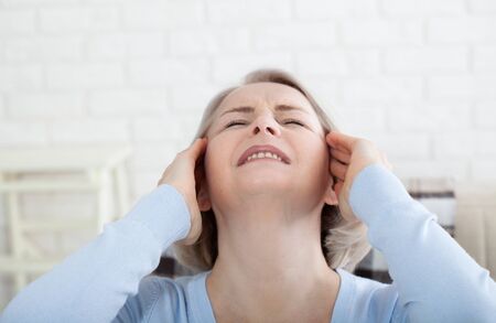 Woman suffering from stress or a headache grimacing in pain as she holds the back of her neck with her other hand to her temple, with copyspace. Concept photo with indicating location of pain.の写真素材