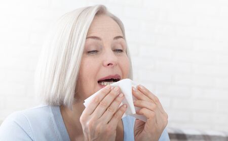 Healthcare, cold, allergy and people concept, sick woman blowing her runny nose in paper tissue on white backgroundの写真素材