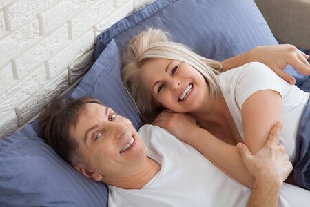 Mature heterosexual beautiful couple lying on bed in bedroomの写真素材