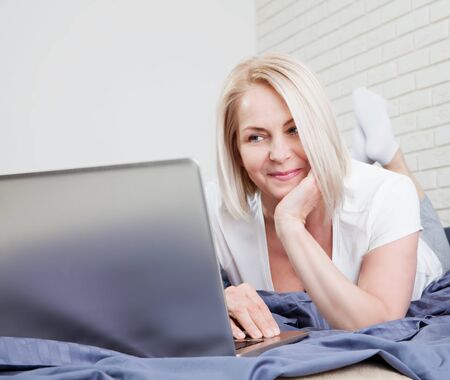 Woman using laptop in home bedroom. Guy lying on bed and typing with notebook computer. Person in the morning with modern device, reading emails, sending messages. Telecommuting conceptの写真素材