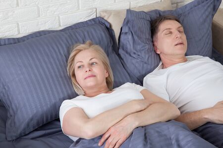 Snoring man. Couple in bed, man snoring and woman can not sleep. Middle age couple in bed at home.の写真素材