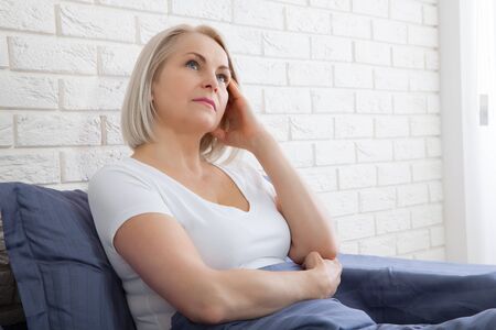 Pensive woman sitting on the bed at homeの写真素材