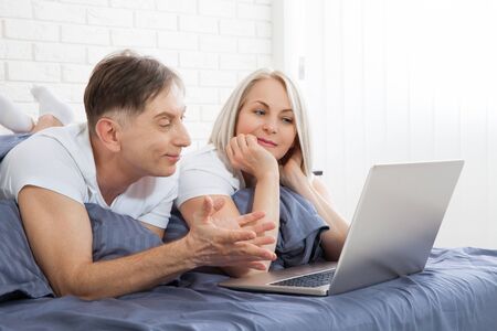 Cute couple relaxing on bed using laptop at home in the bedroomの写真素材