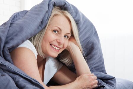 Happy woman hiding under the duvet in bedの写真素材