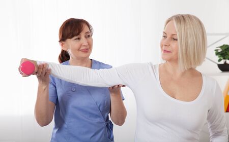 Picture of middle aged woman during rehabilitation in professional clinic. Rehabilitation, physiotherapy with dumbbellsの写真素材