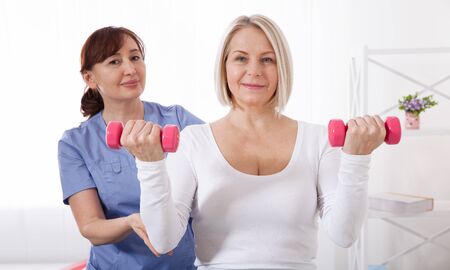A physiotherapist helps an older woman recover from an injury through exercise with dumbbells.の写真素材