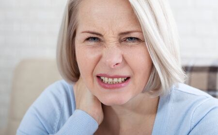 Woman with pain in her neck cloce up, medical shot at home. Concept photo with indicating location of the pain.の写真素材