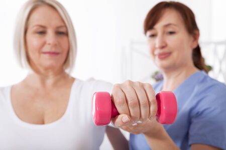 Modern rehabilitation physiotherapy. Physiotherapist helps an middle aged woman recover from an injury through exercise with dumbbells.の写真素材