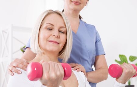 A physiotherapist helps an older woman recover from an injury through exercise with dumbbells.の写真素材