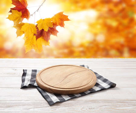 Empty pizza board and table cloth on wooden deck table with napkin. Autumn background.の写真素材