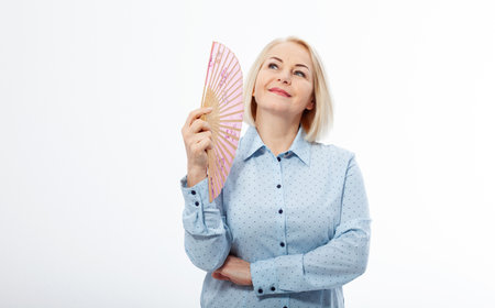 Beautiful middle aged woman with menopause blowing by fan. Hormone replacement therapy and mature woman healthcare. Mid age happy women lifestyle. Senior woman isolated on white backgroundの写真素材