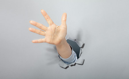 The woman's hand shows with a gesture that everything call for help. Torn hole in gray paper. copyspace.の写真素材