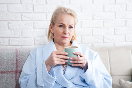Happy beautiful middle aged woman drinking coffee on sofa at home. selective focus.の写真素材
