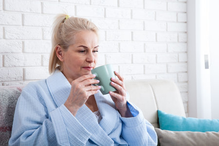 Happy beautiful middle aged woman drinking coffee on sofa at home. selective focus.の写真素材