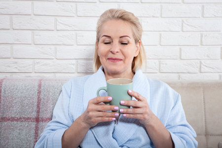 Happy beautiful middle aged woman drinking coffee on sofa at home. selective focus.の写真素材
