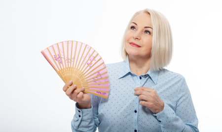 Beautiful middle aged woman with menopause blowing by fan. Hormone replacement therapy and mature woman healthcare. Mid age happy women lifestyle. Senior woman isolated on white.の写真素材