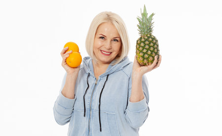 Happy woman with blond hair and beautiful smile holds two oranges and a pineapple in her hands for a healthy diet with vitaminswith. Concept healthy food fruitsの写真素材