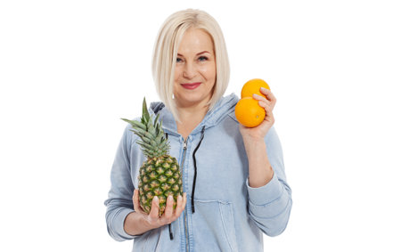 Happy woman with blond hair and beautiful smile holds two oranges and a pineapple in her hands for a healthy diet with vitaminswith. Concept healthy food fruitsの写真素材