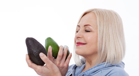 Happy woman with blond hair and beautiful smile holds avocado in her hands for a healthy diet with vitaminswith. Concept healthy food fruitsの写真素材