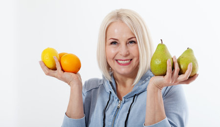 Happy woman with blond hair and beautiful smile holds two oranges, lemon and a pears in her hands for a healthy diet with vitaminswith. Concept healthy food fruitsの写真素材