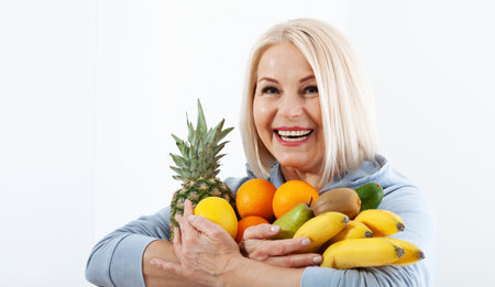 Happy middle aged woman with blond hair and beautiful smile holds products from the store in paper bag of vegetables in her hands for a healthy diet with vitaminswith.の写真素材