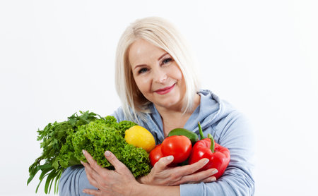 Happy woman with blond hair and beautiful smile holds a bag of vegetables and herbs red pepper and green lettuce in her hands for a healthy diet. Concept healthy food vegetableの写真素材