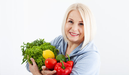 Happy woman with blond hair and beautiful smile holds a vegetables and herbs red pepper and green lettuce in her hands for a healthy diet. The concept of healthy eating vegetables.の写真素材