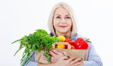 Happy woman with blond hair and beautiful smile holds a bag of vegetables and herbs red pepper and green lettuce in her hands for a healthy diet with vitaminswith. Concept healthy food vegetableの写真素材