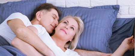 Couple in bed. Man and woman are enjoying spending time together while lying in bed. Happy middle aged couple in bedroom.の写真素材