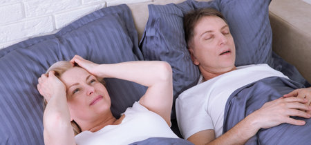Snoring man. Couple in bed, man snoring and woman can not sleep. Middle age couple in bed at home.の写真素材