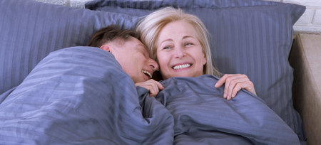 Couple in bed. Man and woman are enjoying spending time together while lying in bed. Happy middle aged couple in bedroom.の写真素材