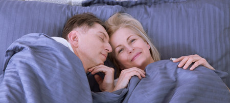 Couple in bed. Man and woman are enjoying spending time together while lying in bed. Happy middle aged couple in bedroom.の写真素材