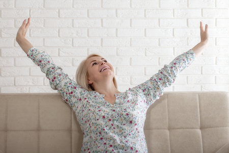 Excited pretty woman raised stretched hands open mouth laughing screaming with joy feels happy sitting on sofa in living room, weekend no stress euphoric lucky lady celebrating lottery win conceptの写真素材