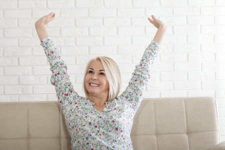 Smiling middle aged mature woman with a stylish haircut, happy old lady posing at home indoor, positive pretty single senior retired female sitting on sofa in living room. headshot portraitの写真素材