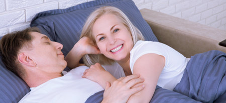 Couple in bed. Man and woman are enjoying spending time together while lying in bed. Happy middle aged couple in bedroom.の写真素材