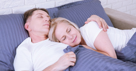 Calm couple sleeping and spooning in bed in bedroom at home.の写真素材