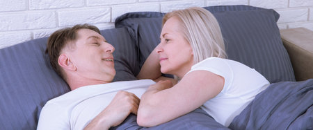 Senior couple at home. Handsome old man and attractive old woman are enjoying spending time together while lying in bed. Selective focus.の写真素材