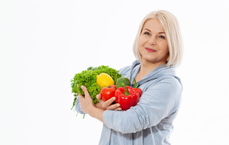 Happy woman with blond hair and beautiful smile holds a vegetables and herbs red pepper and green lettuce in her hands for a healthy diet. The concept of healthy eating vegetables.の写真素材