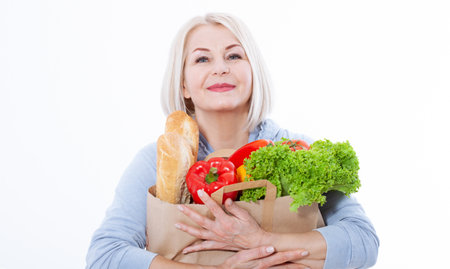 Happy woman with blond hair and beautiful smile holds products from the store in paper bag of vegetables in her hands for a healthy diet with vitaminswith. Concept healthy foodの写真素材