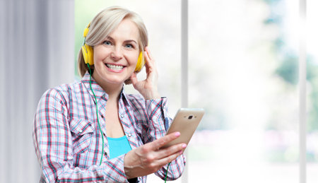 Happy middle aged woman in headphones listening to music from smartphone at home. People, leisure and technology concept .の写真素材