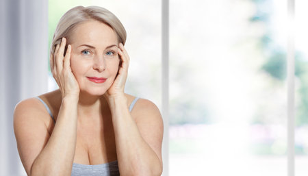 Beautiful middle-aged blonde woman sitting relaxed near the window. Selective focus on face. Realistic images with their own imperfections.の写真素材