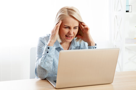 Overwhelmed, sad, and weary middle-aged woman, a businesswoman and freelancer, experiencing headaches and migraines, pondering family, marital, and work-related issues in the office.の写真素材