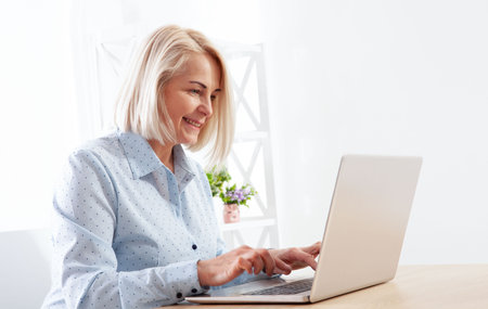 Shot of a content middle-aged woman using her laptop on the table in the office room.の写真素材