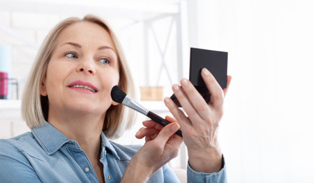 Mirror Magic enchanting image showcasing a woman engrossed in her makeup routine, with the mirror reflecting her poised and confident aura. Woman is doing makeup in front of the mirror at home.の写真素材