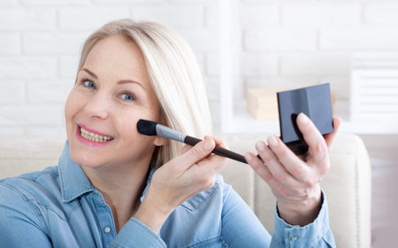 Mirror Magic enchanting image showcasing a woman engrossed in her makeup routine, with the mirror reflecting her poised and confident aura. Woman is doing makeup in front of the mirror at home.の写真素材