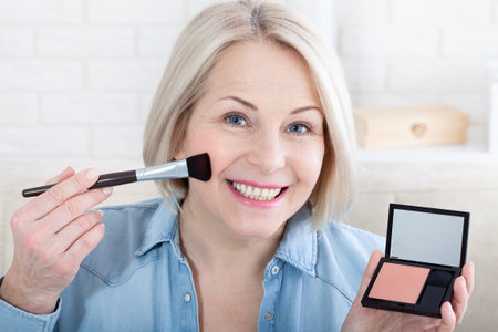 Feminine Grace. A mesmerizing photo capturing a woman's delicate hands expertly adorning her face with makeup, as she prepares for a special occasion. Woman is doing makeup in front of the mirror.の写真素材