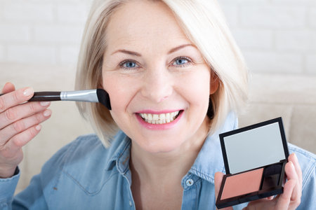 Woman is doing makeup in front of the mirror. Elegance in Reflection. Captivating shot of a woman skillfully applying makeup before a vanity mirror, creating a timeless beauty ritual.の写真素材