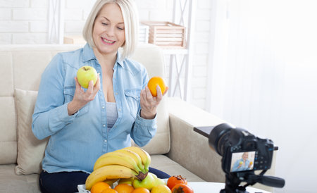 Happy woman shows fruits to the camera at home.の写真素材