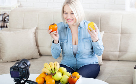 Happy woman shows fruits to the camera at home.の写真素材